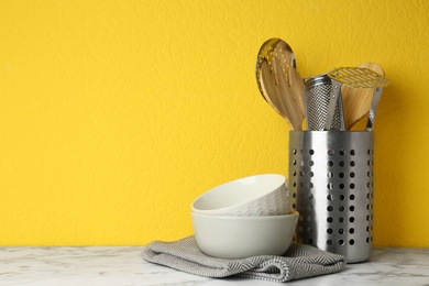 Photo of Different kitchen utensils on marble table against yellow background. Space for text