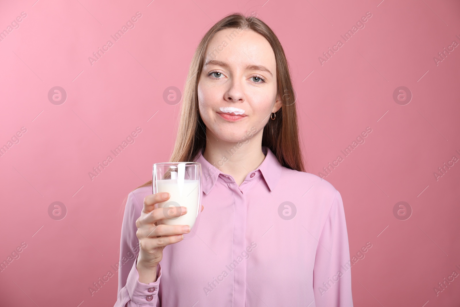 Photo of Cute woman with milk mustache holding glass of tasty dairy drink on pink background