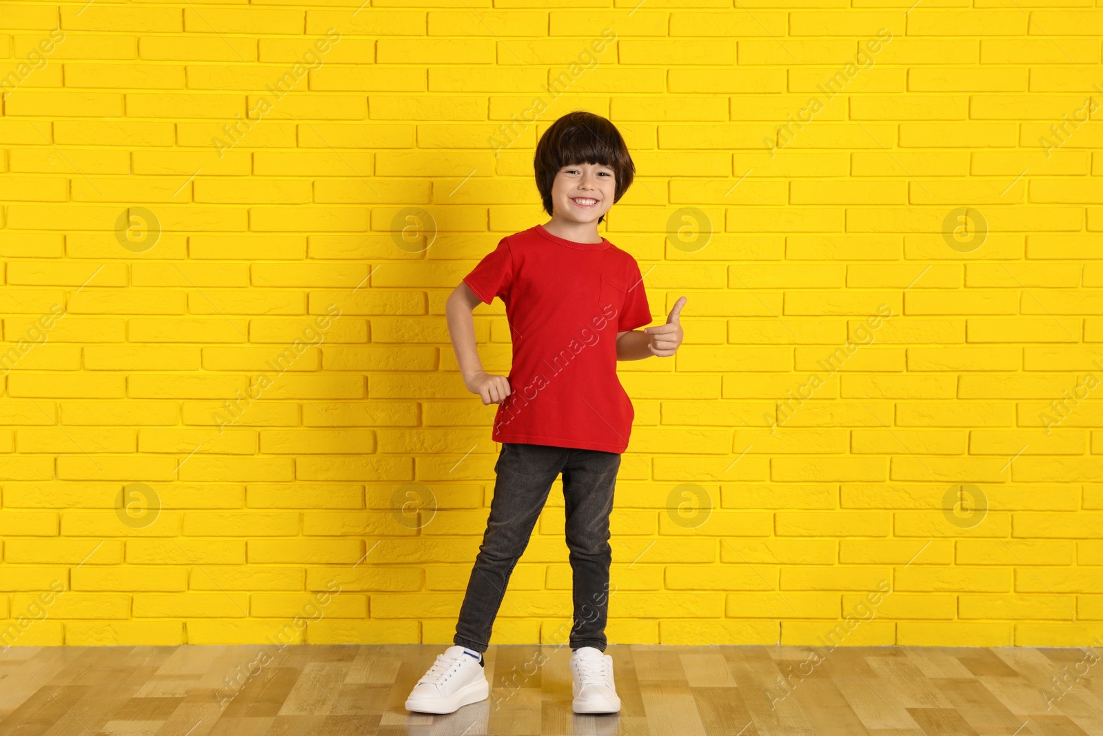 Photo of Cute little boy near yellow brick wall indoors