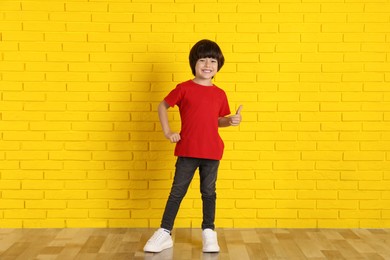 Cute little boy near yellow brick wall indoors