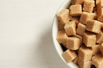 Photo of Brown sugar cubes on white wooden table, top view. Space for text
