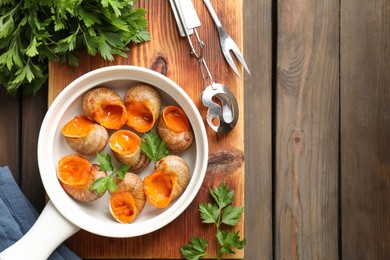 Delicious cooked snails served on wooden table, flat lay. Space for text