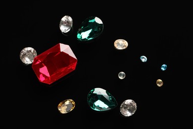 Different beautiful gemstones for jewelry on black background, flat lay