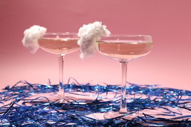 Photo of Tasty cocktails in glasses decorated with cotton candy and blue shiny streamers on pink background