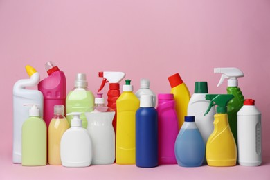 Photo of Many bottles of different detergents on pink background. Cleaning supplies