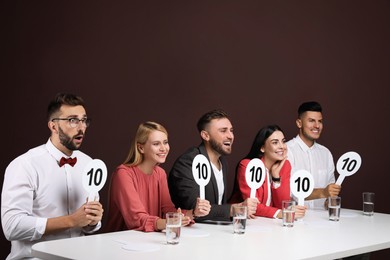 Photo of Panel of judges holding signs with highest score at table on brown background