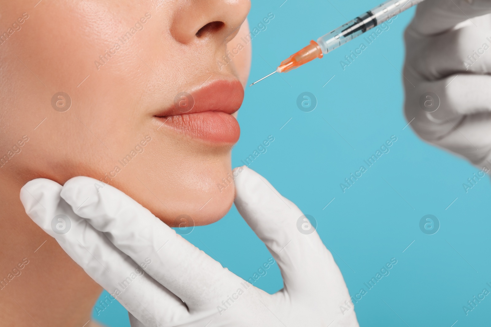 Photo of Doctor giving lips injection to young woman on light blue background, closeup. Cosmetic surgery