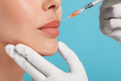 Photo of Doctor giving lips injection to young woman on light blue background, closeup. Cosmetic surgery