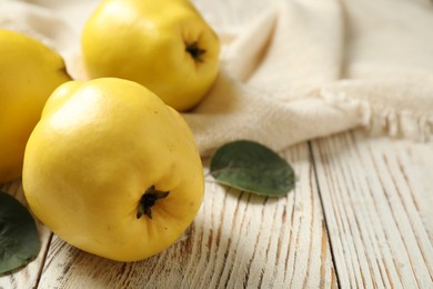Fresh ripe organic quinces with leaves on white wooden table, closeup. Space for text