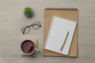 Ballpoint pen, notebooks and cup of tea on wooden table, flat lay