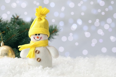 Photo of Snowman toy on snow against blurred festive lights. Space for text