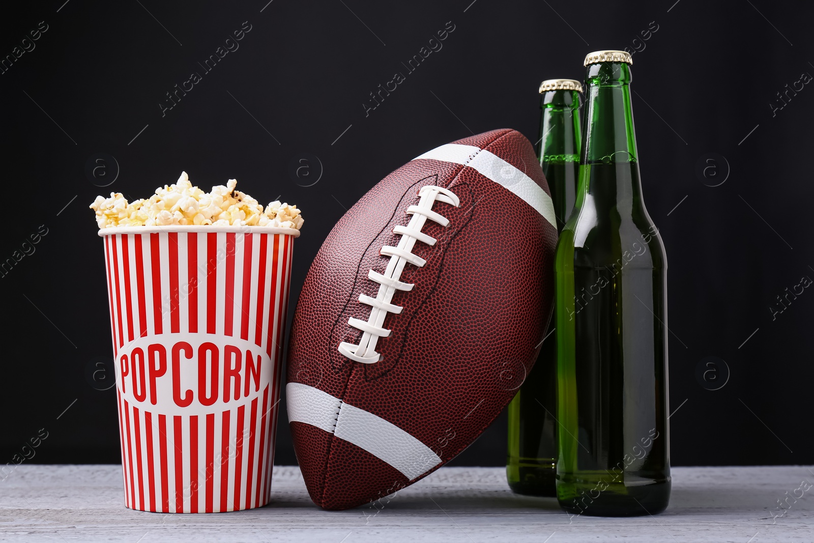 Photo of American football ball with popcorn and beer on grey wooden table