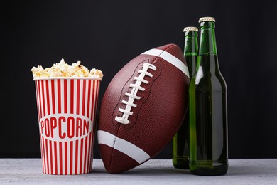 Photo of American football ball with popcorn and beer on grey wooden table