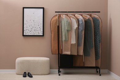 Photo of Garment bags with clothes hanging on rack in room