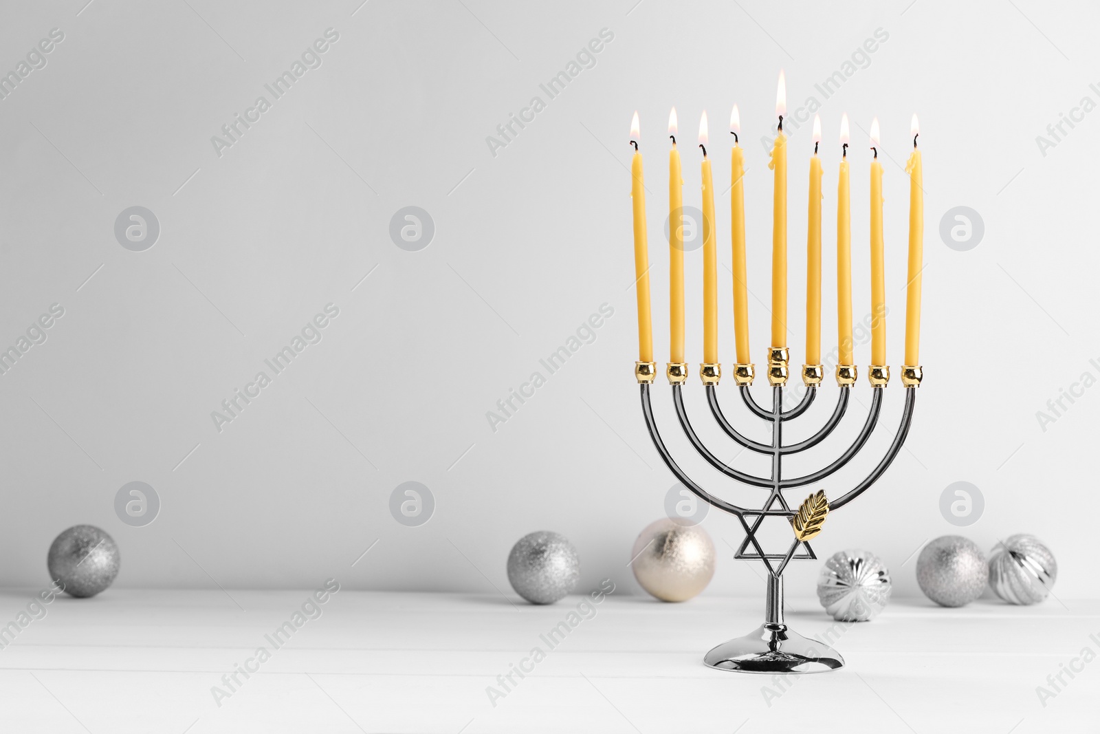 Photo of Hanukkah celebration. Menorah with burning candles and holiday ornaments on white wooden table, space for text