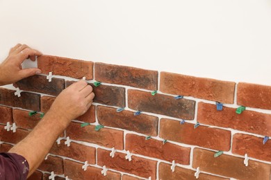 Photo of Professional builder installing new brown decorative bricks on wall, closeup