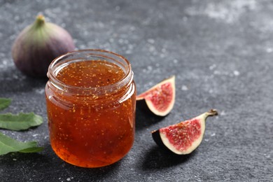 Photo of Jar with tasty sweet jam and fresh figs on black textured table, closeup. Space for text