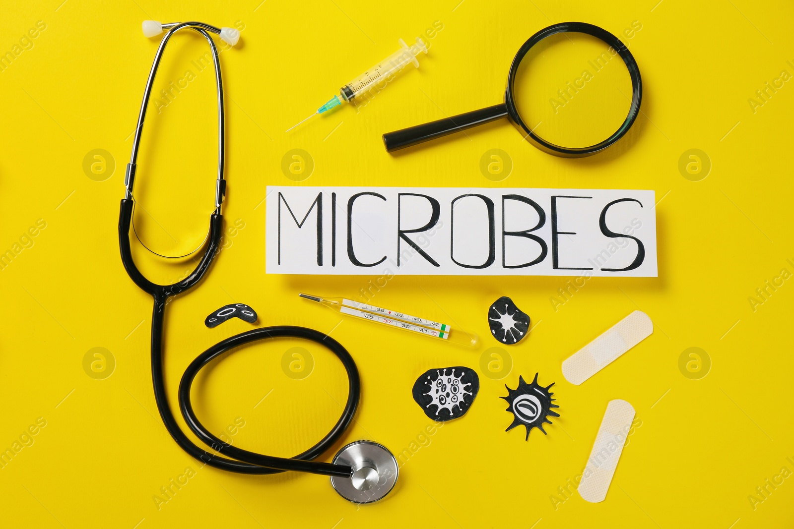 Photo of Card with word Microbes, magnifying glass, syringe, stethoscope and thermometer on yellow background, flat lay