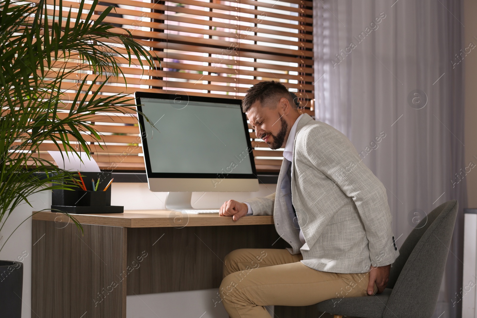 Photo of Man suffering from hemorrhoid at workplace in office