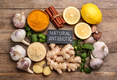 Photo of Different fresh products and card with phrase Natural Antibiotic on wooden table, flat lay