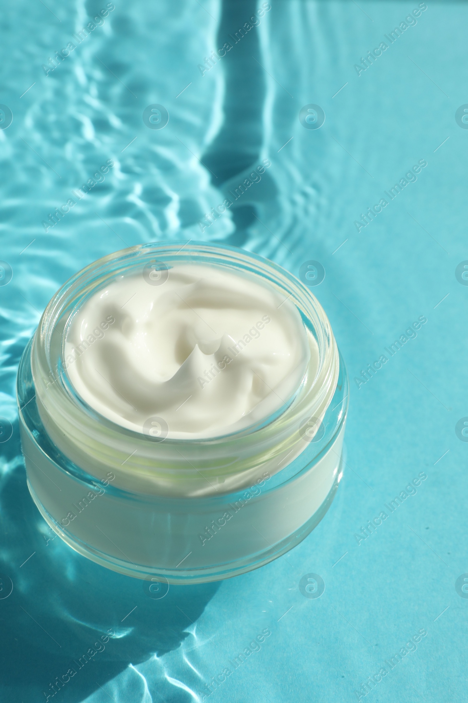 Photo of Jar with moisturizing cream in water on light blue background