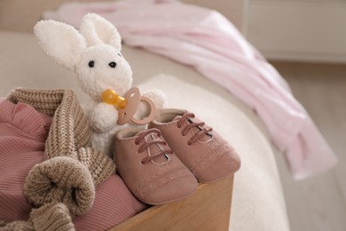 Photo of Wooden crate with children's clothes, shoes and toy bunny on sofa in room. Space for text