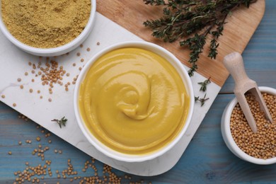 Photo of Delicious mustard, seeds and thyme on light blue wooden table, flat lay