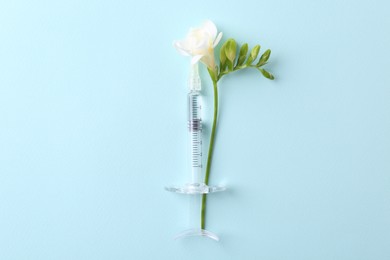 Cosmetology. Medical syringe and freesia flower on light blue background, top view