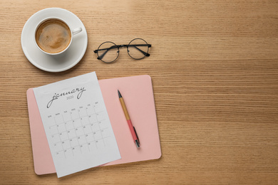 Flat lay composition with calendar and cup of coffee on wooden table. Space for text
