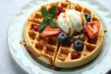 Delicious Belgian waffles with ice cream, berries and caramel sauce served on grey table, closeup