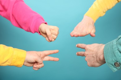 People playing rock, paper and scissors on light blue background, closeup