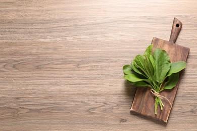 Green broadleaf plantain leaves on wooden table, top view. Space for text