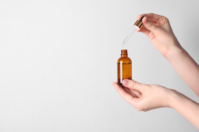 Woman holding bottle of cosmetic oil on light background, closeup. Space for text