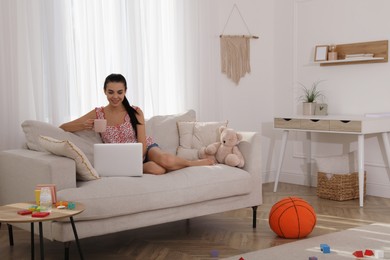 Photo of Happy young mother with cup of coffee and laptop resting in messy living room