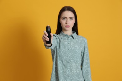 Photo of Young woman using pepper spray on yellow background