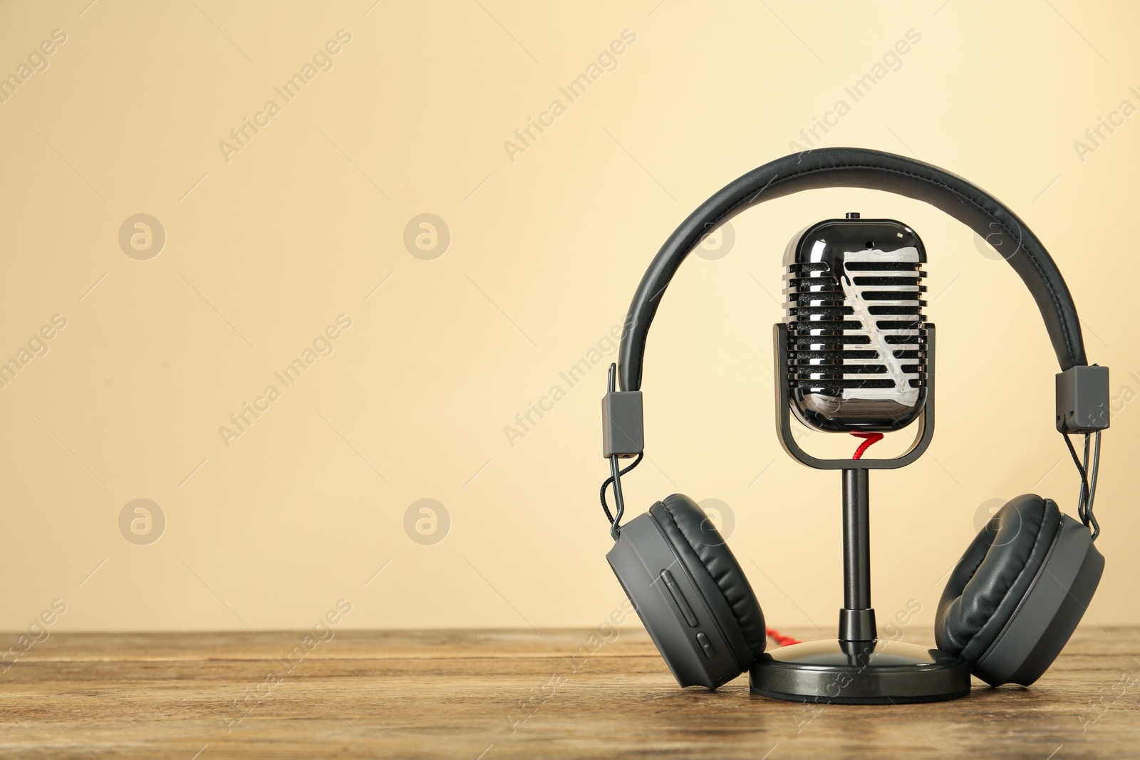 Photo of Microphone and modern headphones on wooden table against beige background, space for text