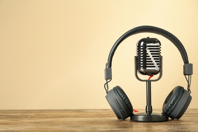 Photo of Microphone and modern headphones on wooden table against beige background, space for text