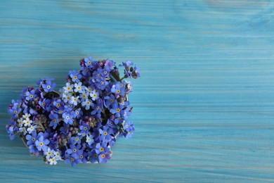 Photo of Heart of beautiful forget-me-not flowers on light blue wooden table, top view. Space for text