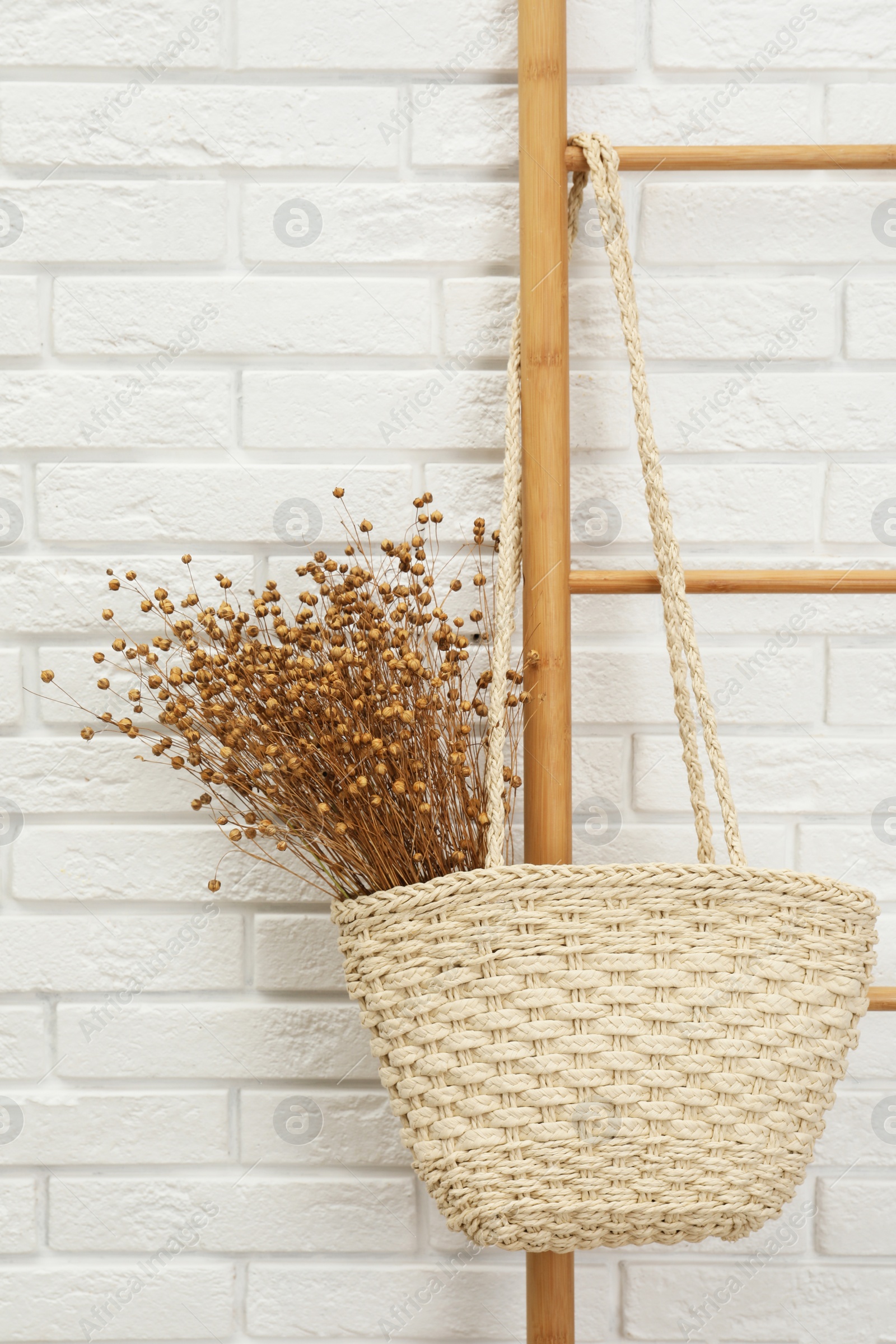 Photo of Stylish beach bag with beautiful dried flowers hanging  on wooden ladder