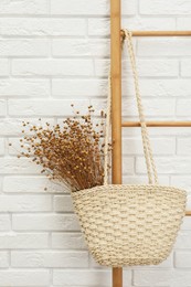 Photo of Stylish beach bag with beautiful dried flowers hanging  on wooden ladder