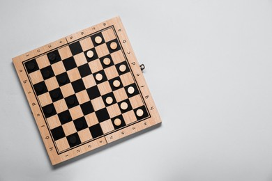 Wooden checkerboard with game pieces on light grey background, top view. Space for text