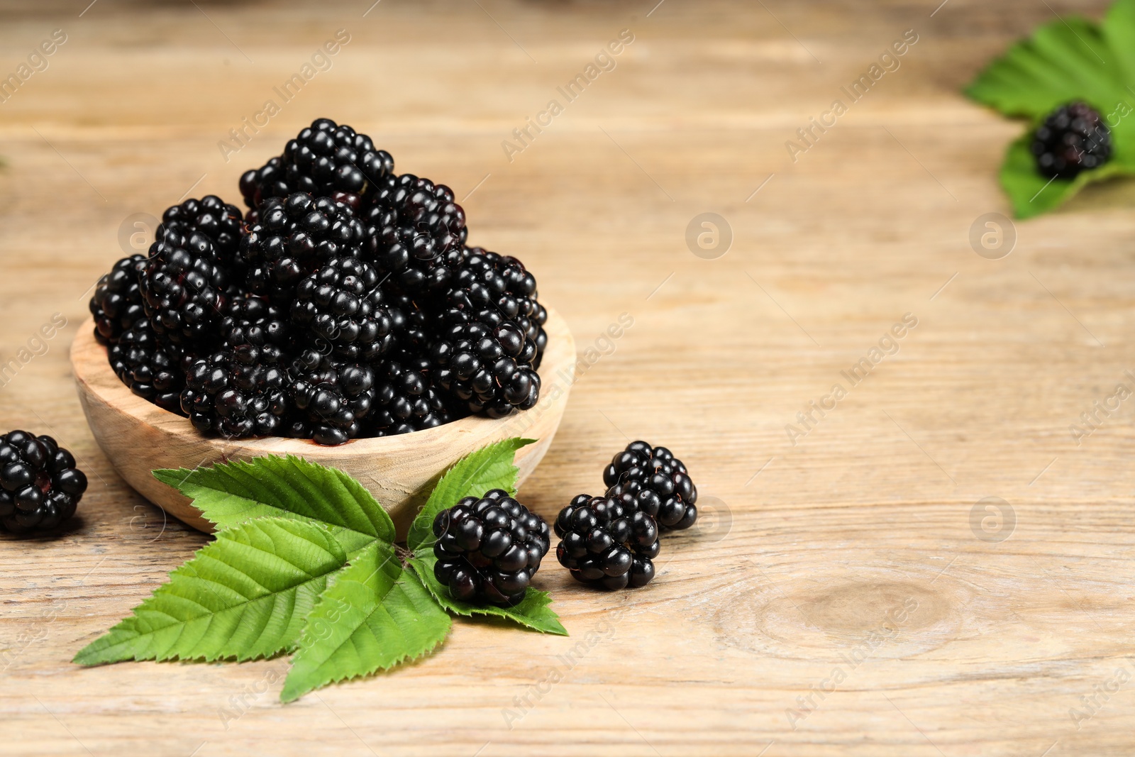Photo of Ripe blackberries and green leaves on wooden table, closeup. Space for text