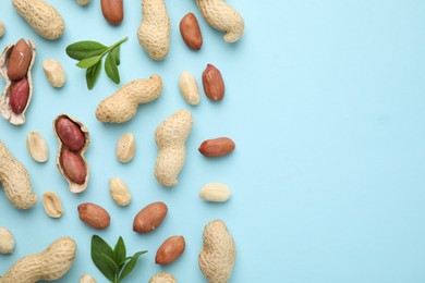 Photo of Fresh peanuts and leaves on light blue table, flat lay. Space for text