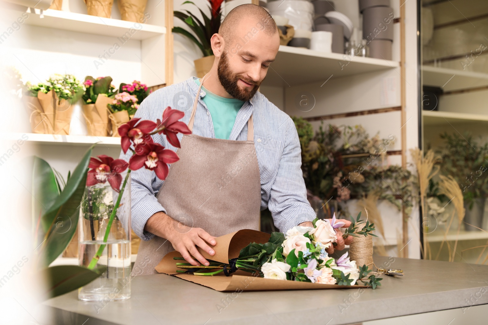 Photo of Florist making bouquet with fresh flowers at table in shop