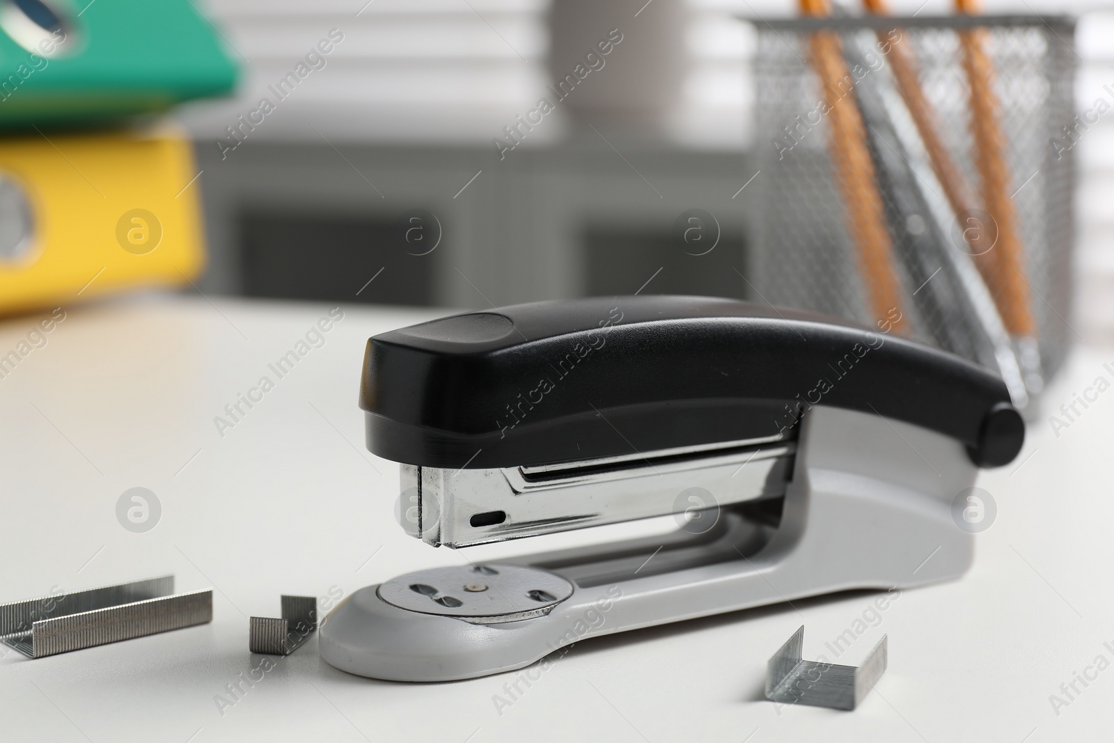 Photo of Stapler and metal staples on white table indoors, closeup