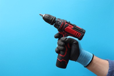 Handyman holding electric screwdriver on light blue background, closeup. Space for text