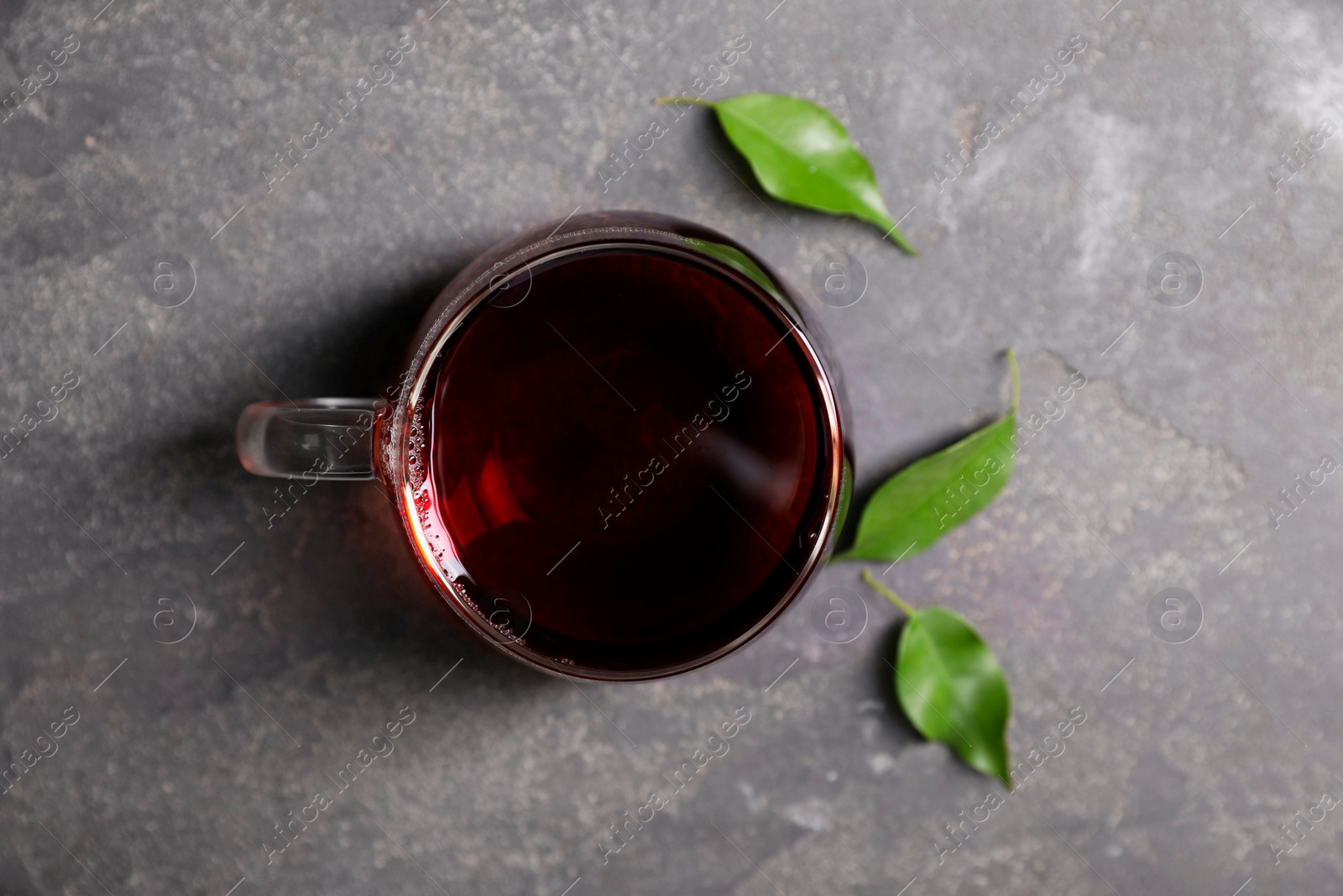 Photo of Tasty hot tea in cup and leaves on grey table, top view