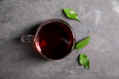 Photo of Tasty hot tea in cup and leaves on grey table, top view