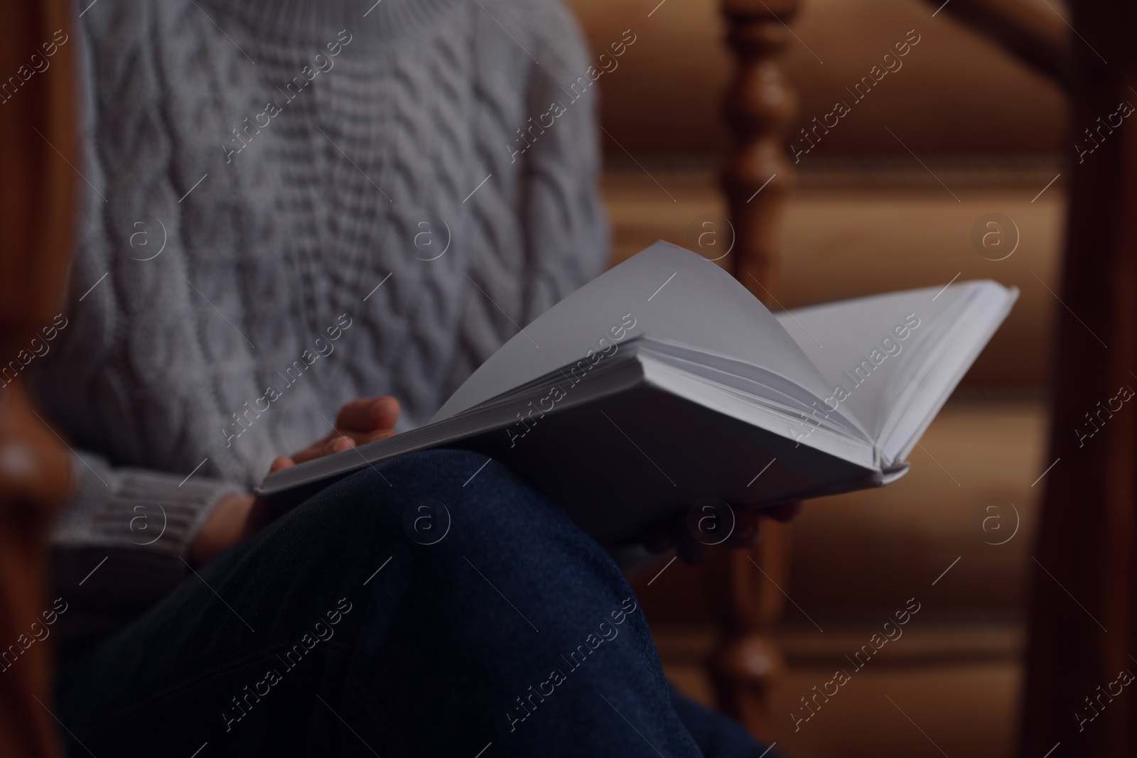 Photo of Woman reading book on stairs at home, closeup