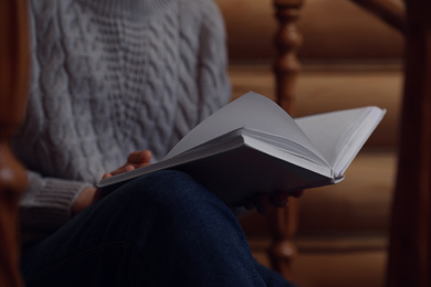 Woman reading book on stairs at home, closeup